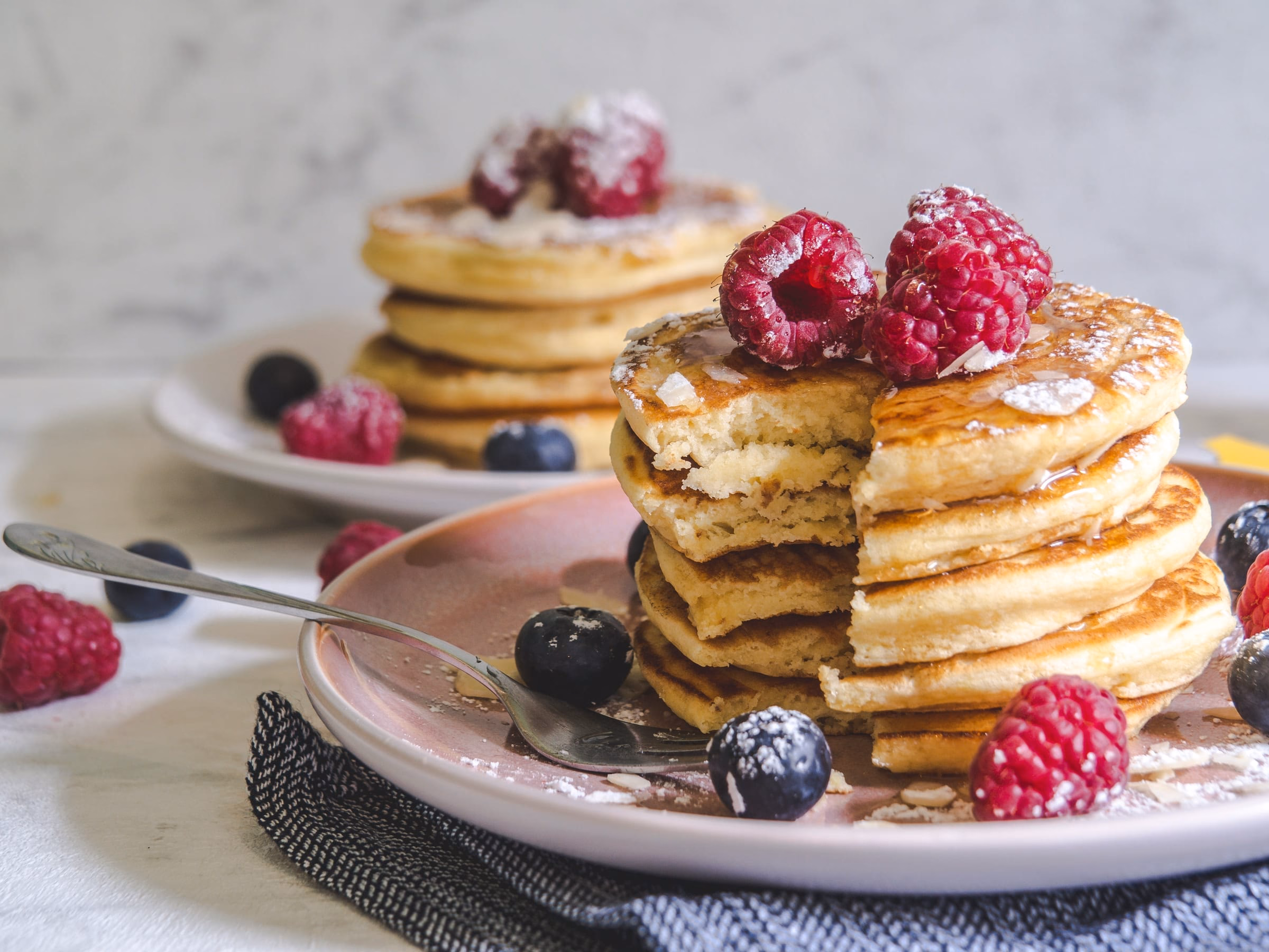 Stapel Pancakes mit Himbeeren und Heidelbeeren auf einem hellen Teller