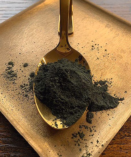 Goldener Loeffel mit dunkelgruenem Spirulina-Pulver auf einem Holzbrett